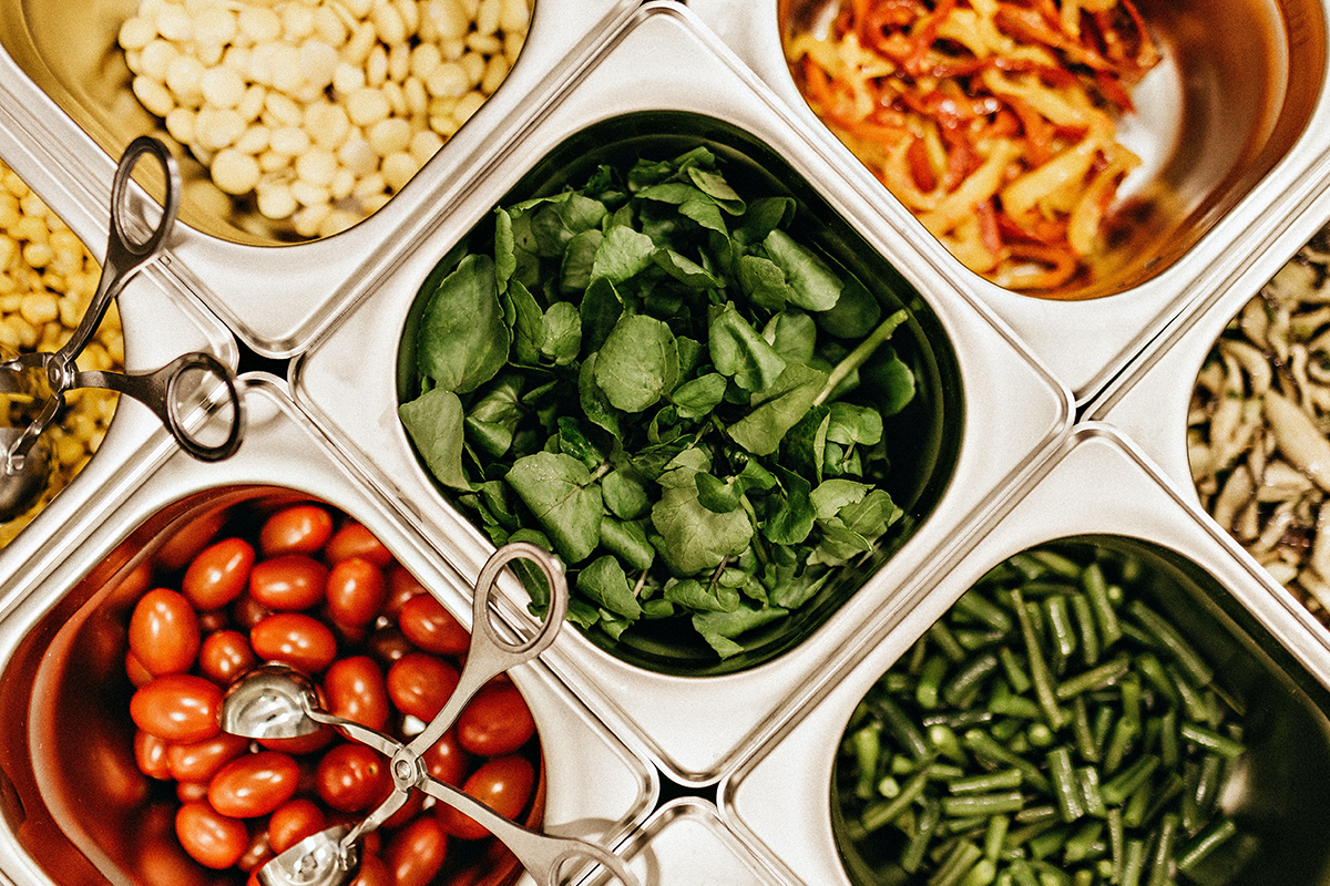 A salad or food bar consisting of tomatoes, corn, spinach, green beans, bell peppers, and mushrooms.