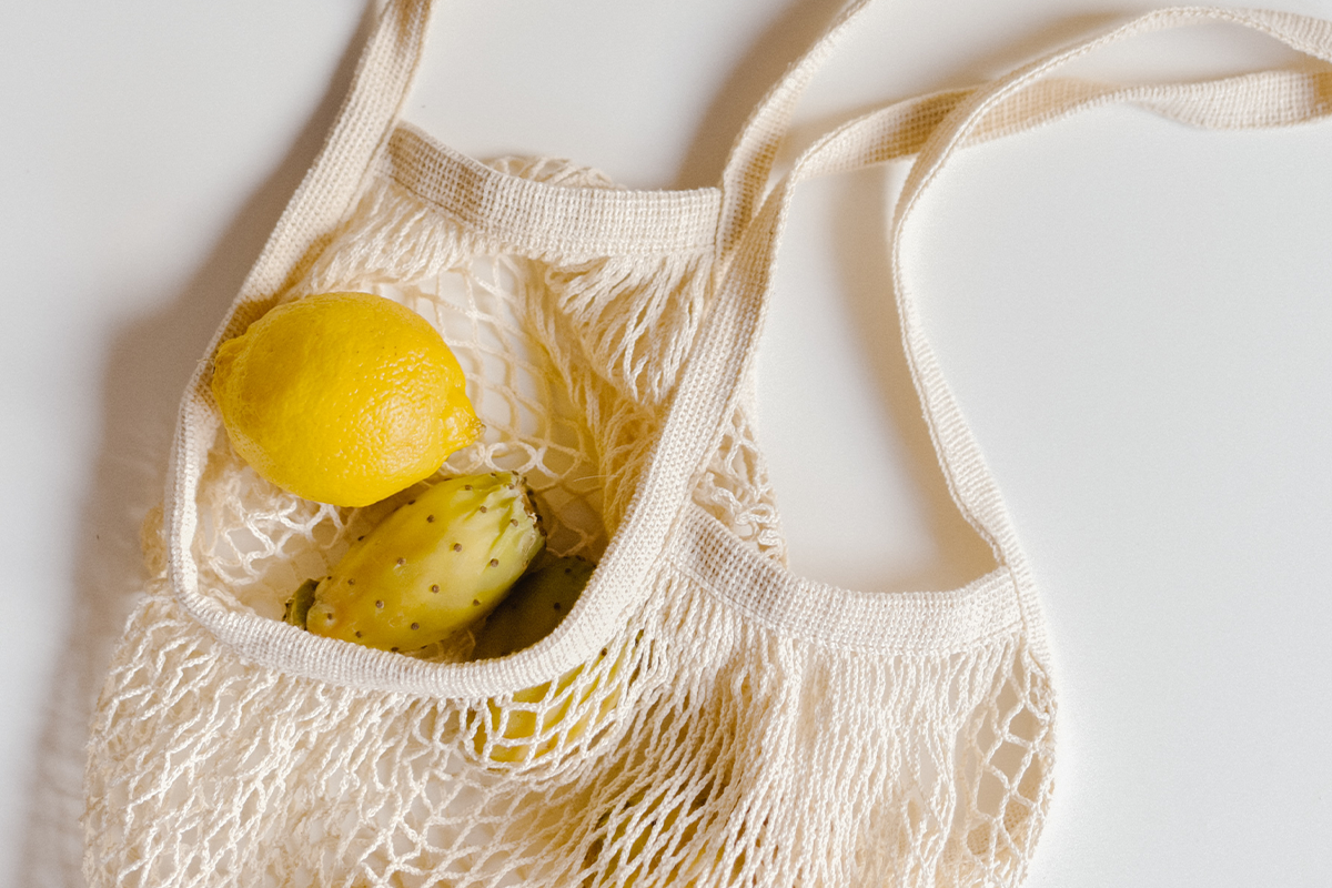 A reusable produce bag filled with lemons and dragonfruit laying against a white background.